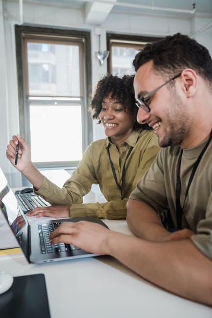 Two smiling people at a table working on their computers after fixing a slow Mac.